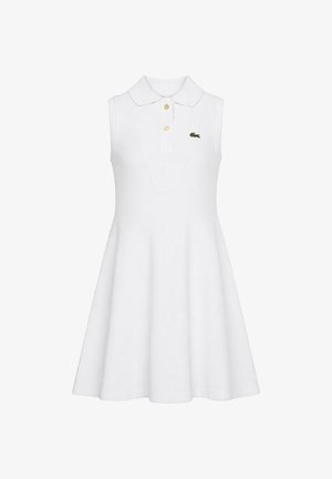 Mouwloze witte polojurk met uitlopende rok, twee knopen en een klein groen krokodillenlogo op de borst.