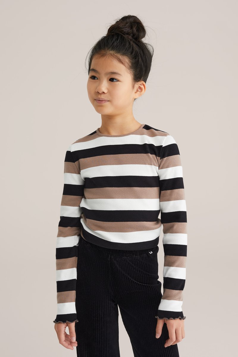 Svītrots garo piedurkņu krekls melnā, baltā un brūnā krāsā. Rievota tekstūra ar apaļu kaklu un viļņotām aprocēm. Apvienots ar melnajām kordūru biksēm.