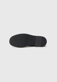 Black shoe sole with a textured, ribbed surface. Features a flat heel and a rectangular accent in the middle. Smooth edge detailing.