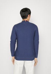 Maglione lavorato a maglia blu navy con un motivo testurizzato, collo rotondo, polsini e orlo a coste. Presenta un accento tricolore sul colletto.