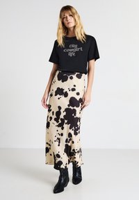 T-shirt noir avec texte brillant, associé à une longue jupe beige avec un motif de taches noires. Complété par des bottines noires.