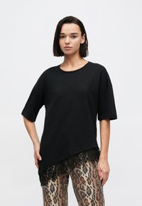 Černé oversize tričko s krátkými rukávy a krajkovým lemováním. Nošeno s kalhotami s leopardím vzorem pro kontrast.