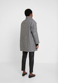Grijze houndstooth jas met een hoge kraag, losse pasvorm en verlaagde schouders, gecombineerd met zwarte leren broeken en platte schoenen. Zachte textuur.