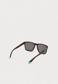 Ορθογώνια γυαλιά ηλίου από καρώ σε σκούρο χρώμα με σκουρόχρωμα πολωμένα φακούς και τιρκουάζ άκρες στα πόδια, σε απλό λευκό φόντο.