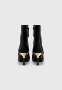 Stivali ankle neri in pelle con punta affusolata, dettagli in metallo dorato e tacco alto sottile. Presentano una texture liscia e chiusura con zip.