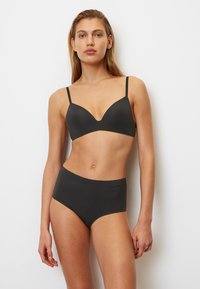 Bralette noire avec un design en V et des fines bretelles, associée à une culotte noire taille haute. Texture lisse, style minimaliste et sans matériel visible.