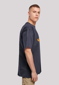Marineblå bomulls t-skjorte med korte ermer, rund hals og et gult grafisk design på brystet. Relaxed fit med sidefuger synlige.