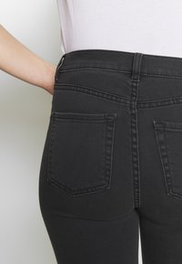 Vaqueros de mezclilla negra con forma ajustada, que cuentan con dos bolsillos traseros, detalles de costura sutiles y una cinturilla alta.