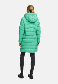 Mint green puffer coat with a detachable hood, chevron pattern stitching, side pockets, and a mid-thigh length. Paired with dark jeans and boots.