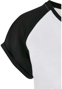 T-paita lyhyillä hihoilla, jossa on musta raglan-kuvio. Pääosa on valkoinen. Kangas vaikuttaa pehmeältä ja sileäpintaiselta. Käännetyt hihojen suut.