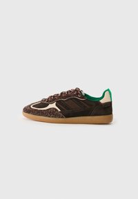 Scarpa con tomaia in tessuto marrone, accenti beige e colletto verde. Profilo basso con suola in gomma beige e lacci marroni su uno sfondo scuro.