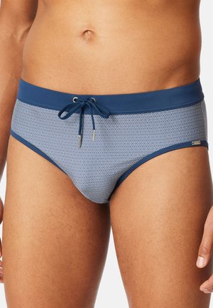 Close-up of a man's midsection wearing blue and white patterned swim briefs with a solid blue waistband and front drawstring.
