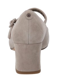 Beige mockaskinnsklackskor med rund tå, en bakrem och dekorativ rosett på sidan. Texturerad yta med sydda detaljer.