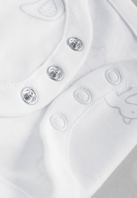 White cotton onesie featuring snap closures. Rounded collar with silver hardware, soft texture, and subtle printed patterns of animals.