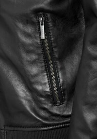 Zwarte leren jas met een zilveren rits aan de linkerkant, een gestructureerd oppervlak en geribbelde manchetten.
