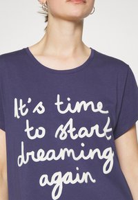 Fioletowa bawełniana koszulka z krótkim rękawem, na której znajduje się biały, ręcznie napisany tekst: "Czas zacząć znów marzyć."