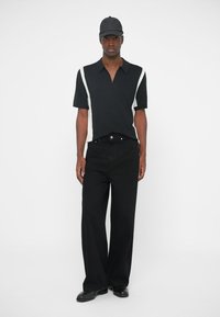 Polo negru cu mânecă scurtă, cu dungi albe pe laterale, purtat cu blugi largi negri și o șapcă neagră. Textură netedă și croială ajustată.