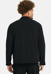 Camisa negra de manga larga con corte recto. Presenta una textura acanalada y detalles con logotipo en la parte posterior. Diseño simple con acentos de puños abotonados.