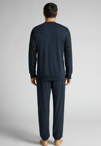 Námořnický relaxační set se skládá z trička s dlouhým rukávem, které má na rukávech kostkované detaily, a odpovídajících kalhot s elastickým pasem. Měkký materiál, uvolněný střih.