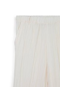 Tessuto crema chiaro, testurizzato e plissettato, con una cinturina elastica ampia. Il tessuto scivola dolcemente, con un leggero luccichio.