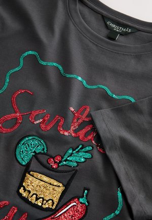 Grå tyg-T-shirt med färgglada paljettdekorerade grafik med jultema: "Tomten", ett glas och järnek med röda och gröna accenter.