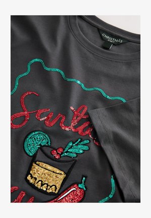 Grå tyg-T-shirt med färgglada paljettdekorerade grafik med jultema: "Tomten", ett glas och järnek med röda och gröna accenter.