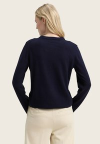 Marineblauwe gebreide trui met een ronde hals, ribbels aan de mouwen en onderkant; heeft een zachte textuur en een casual pasvorm. Eenvoudig ontwerp zonder patronen.