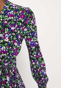 Blommig klänning med svart bakgrund och gröna, lila och vita blommor. Långa puffärmar och knytband i midjan. Mjuk tygtextur.