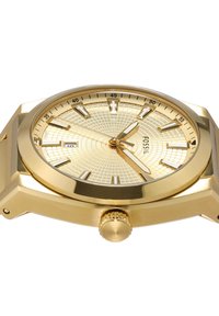Reloj de pulsera Fossil dorado con esfera de patrón geométrico, marcadores de hora luminiscentes, indicación de fecha a las 9 en punto y tres manecillas doradas que marcan las 2:23:59.