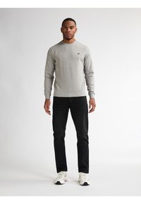 Grijze crewneck sweatshirt met geribde manchetten en zoom, gecombineerd met zwarte broeken en witte sneakers. Eenvoudig ontwerp, geen zichtbare patronen of logo's.