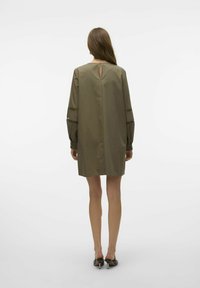 Olijfgroen shift-jurk met lange mouwen, een sleutelgatenrugdetail en opengewerkte accenten nabij de polsen. Gladde stof, knie-lange pasvorm.