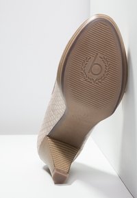 Chaussure à talon haut nude avec un motif texturé en peau de serpent. Présente un talon beige rayé et une semelle en caoutchouc avec un logo de marque et la taille 37.