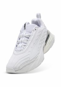 Baskets de sport blanches avec mesh texturé, semelle épaisse, fermeture à lacets à l'avant, languette au talon et accent argenté près de la semelle.