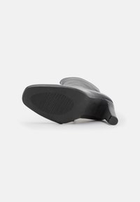 Zapato de tacón alto negro con exterior de cuero suave, puntera redondeada y suela de goma texturizada con canales horizontales.