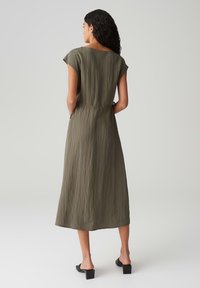 Olivgrünes Midikleid aus leichtem, strukturiertem Stoff. Mit kurzen Ärmeln, tailliertem Schnitt und zwei seitlichen Taschen.