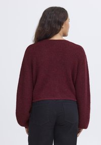 Maglione borgogna cropped con un design a maglia testurizzata. Presenta maniche larghe e un collo ampio, abbinato a pantaloni neri aderenti.