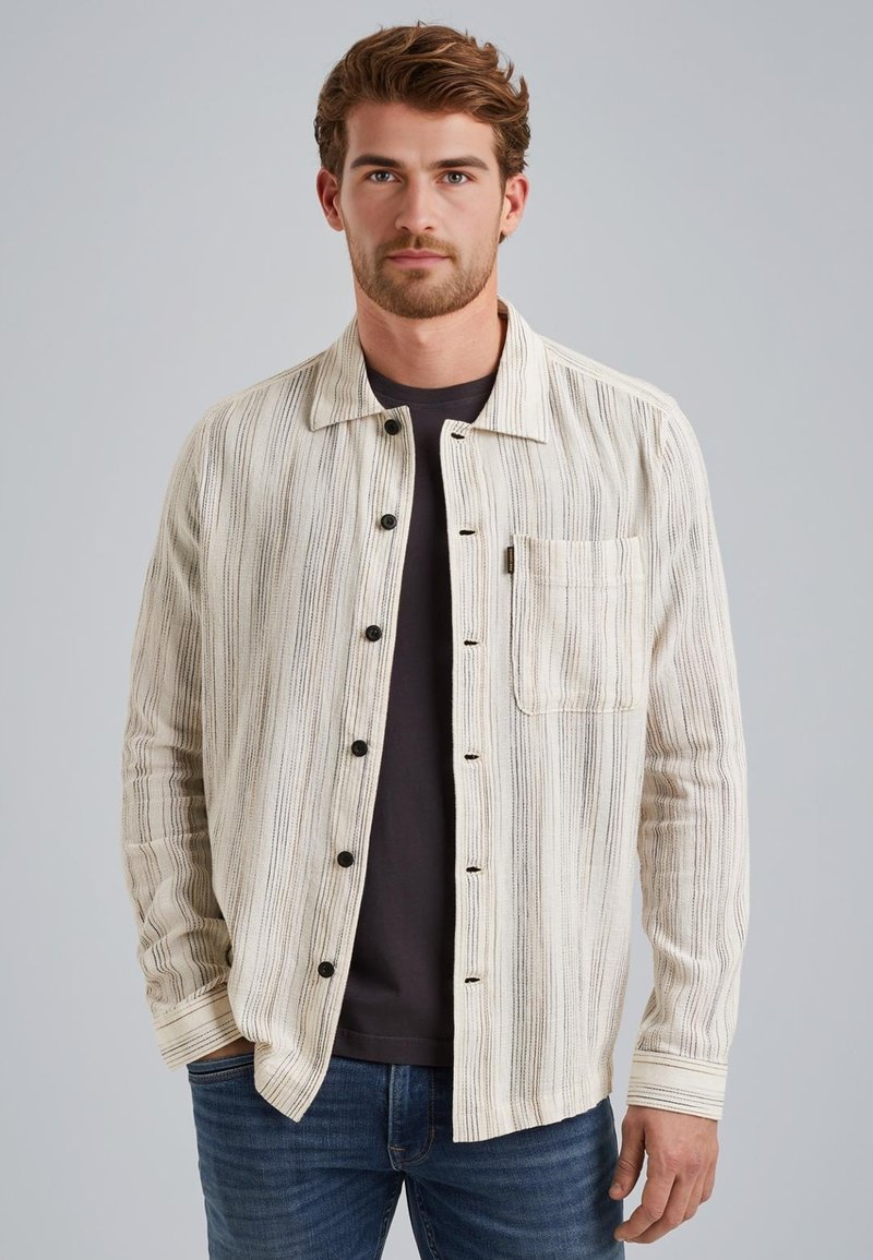 Chemise à manches longues rayée en blanc cassé et noir, avec fermeture à boutons, poche poitrine et tissu texturé. Portée par-dessus un t-shirt noir.