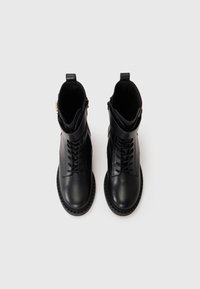 Black leather ankle boots with lace-up design, side zipper, and rubber sole. Features smooth texture, padded collar, and minimal hardware accents.