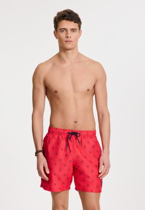 Pantalones de baño rojos con cintura ajustable, que presentan un patrón de hojas en azul marino. Hechos de un tejido ligero para mayor comodidad y secado rápido.