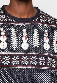 Maglione lavorato a maglia blu navy con un motivo invernale che presenta pupazzi di neve, alberi e fiocchi di neve in bianco e rosso. Design classico con scollo a girocollo.