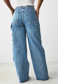 Jeans cargo a gamba larga in azzurro chiaro con multiple tasche, orlo sfrangiato e texture in denim sbiadito, caratterizzati da un classico design a cinque tasche.