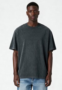 Tumši pelēkas krāsas pārāk liela T-kreklu ar īsām piedurknēm, apaļu kakla izgriezumu un mīkstu tekstūru. Valkāts ar gaiši ziliem džinsiem.