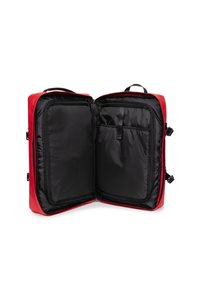Borsa da viaggio rossa con un'esterno lucido, apertura con zip e interno nero. Presenta scomparti per l'organizzazione e doppi manici per il trasporto.