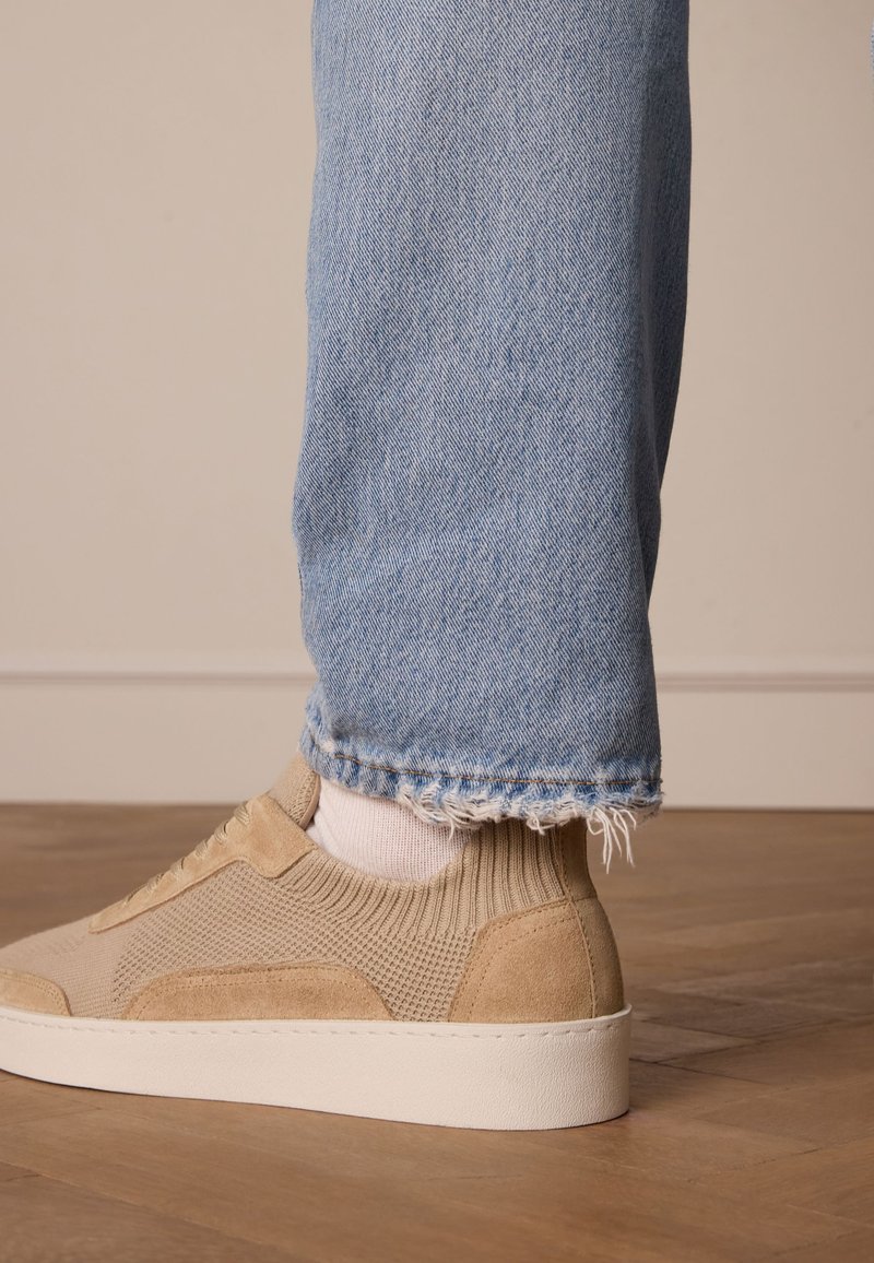 Sneakers beige realizzati in mesh testurizzato e suede, con suola bianca. Indossati con jeans azzurri sfilacciati e calzini bianchi.