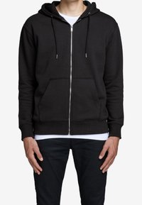 Svart zip-up hoodie med huva, frampocketar och dragsnoddar, tillverkad av ett mjukt material. Har en ribbad nederkant och ärmar.