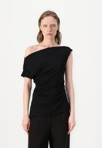 Melna blūze bez pleciem ar plūstošu audumu, īsām piedurknēm un piegulīgu siluetu. Mīksta tekstūra un gluda apdare. Apvienota ar platām biksēm.