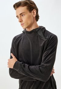 Fleece-pullover i mörkgrått med hög krage, dragkedjedetalj och långa ärmar; mjuk textur och avslappnad passform.