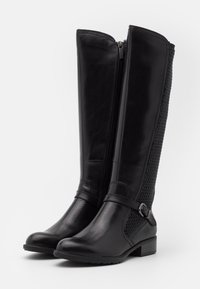 Botas de cuero negras hasta la rodilla con un panel de malla texturizada. Cuentan con un zipper lateral y una correa con detalle de hebilla en el tobillo.