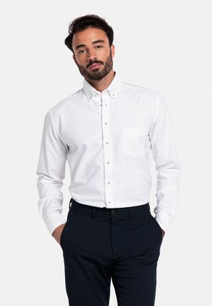 Witte overhemd met een puntige kraag, een enkele borstzak en een subtiele textuur, gecombineerd met donkerblauwe pantalon.