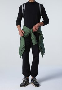 Black long-sleeve shirt, green puffer jacket tied around waist, black jogger pants, and black sneakers with reflective accents and laces.